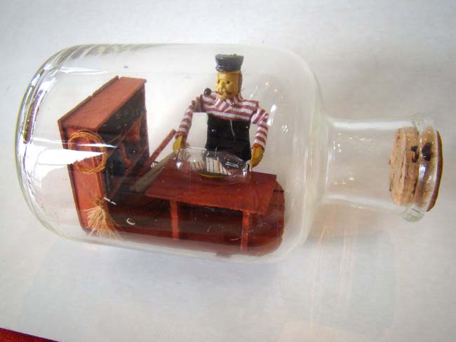 A wonderful small ship-in-a bottle depicting a sailor making a ship-in-a bottle — image 5